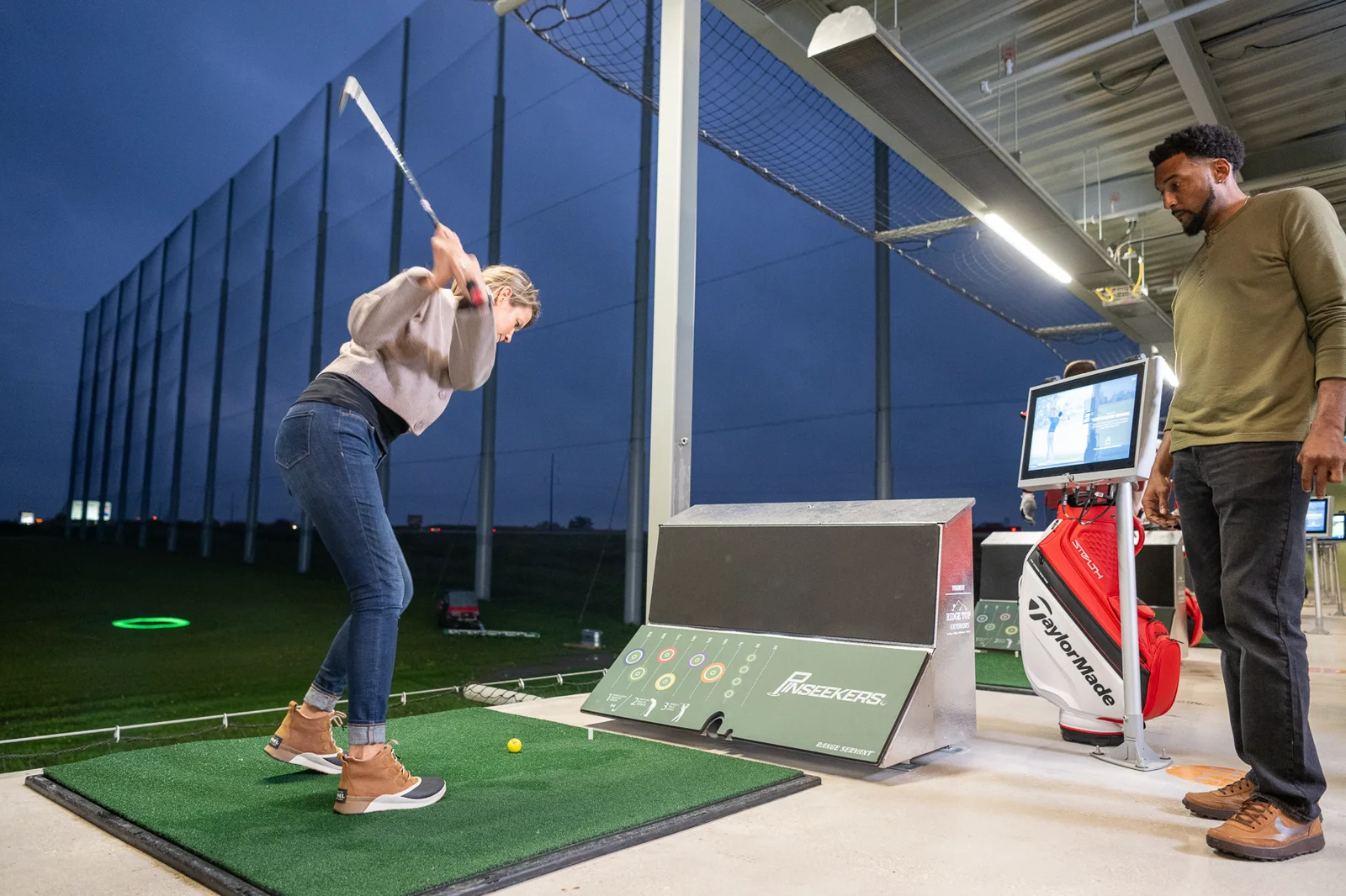 Pinseekers driving bay: a golfer at the tee with overhead SRP infrared heating along the ceiling
