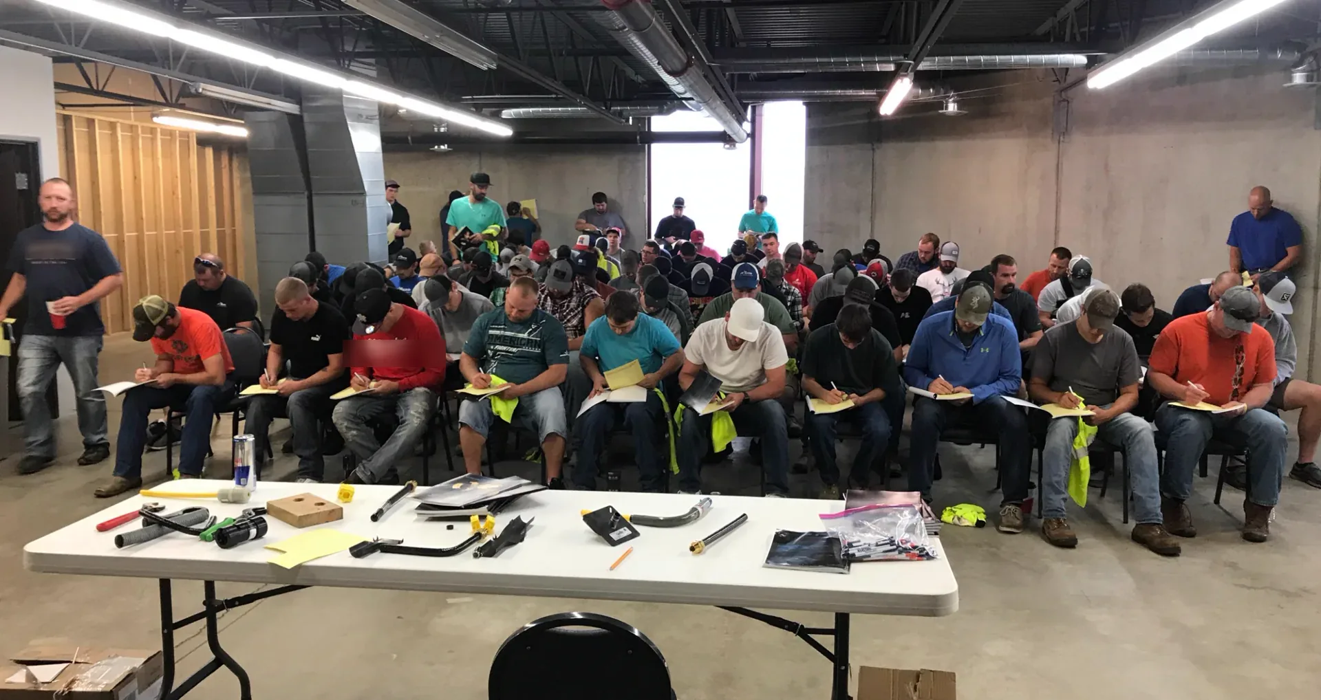 Contractors taking notes at a hands-on product demonstration, with the tools and fittings laid out on a table